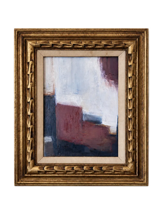 An abstract painting with blocks of white, dusty red, navy, and plum, housed in an ornate gold frame and hung on a light gray wall.