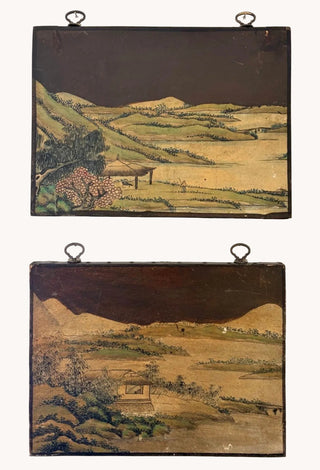 Two vintage hand-painted wooden landscape panels hanging on a white wall, featuring traditional Japanese-style scenery with green hills, golden fields, and dark sky.