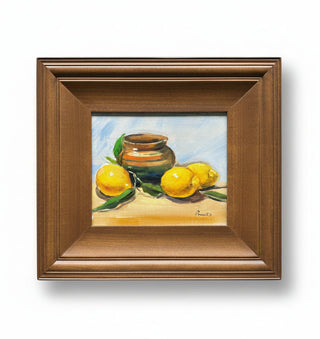 A framed still life painting featuring yellow lemons, green leaves, and a brown ceramic pot on a light blue and beige background, enclosed in a medium brown wooden frame.