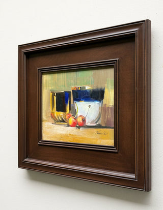 A framed still life painting featuring yellow, blue, and red tones, housed in a dark brown wooden frame and mounted on a light gray wall.
