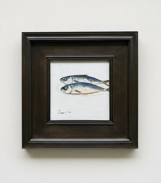 A framed painting of two small blue-gray fish on a white background, set in a dark brown wooden frame and displayed against a light gray wall.