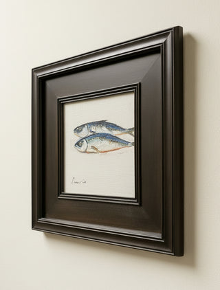 Framed wall art featuring a painted illustration of two silver-blue fish on a white background, housed in a dark brown wooden frame and mounted on a light wall.