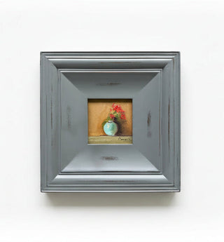 A square framed miniature oil painting featuring a still life of a small blue-green vase with red flowers on a warm brown background, housed in a distressed gray frame.