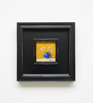 A framed miniature still life painting featuring a vibrant blue vase with white blossoms against a warm yellow background, housed in a thick black frame with a black mat.