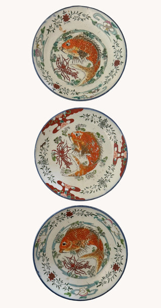 Three ceramic plates with traditional Japanese fish designs, arranged vertically on a dark wooden surface.